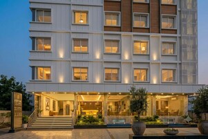 Un hotel de varios pisos con fachada moderna, entrada bien iluminada y un área exterior con jardines.