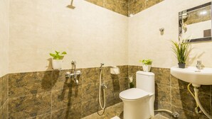 A bathroom with a toilet, sink, shower, and two potted plants.