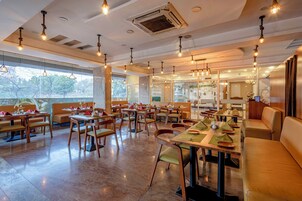 A spacious restaurant with multiple dining areas, large windows, and hanging light fixtures.