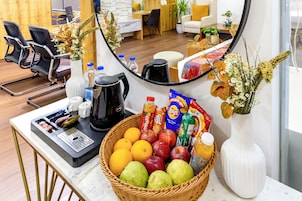 A hotel reception area with a coffee station, a fruit basket, and a mirror reflecting the room.