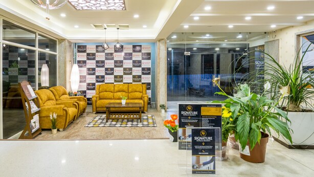 A hotel lobby with a checkered floor, a yellow sofa, a coffee table, and potted plants.