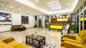 A hotel lobby with a reception desk, sofas, a coffee table, and a decorative ceiling.
