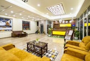 Un hall de hotel con mostrador de recepción, sofás, una mesa de centro y un techo decorativo.