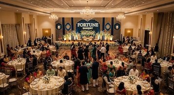 Un salón de banquetes con mesas redondas dispuestas para un evento formal, un escenario con un telón de fondo que dice 'FORTUNE BANQUET' y candelabros.
