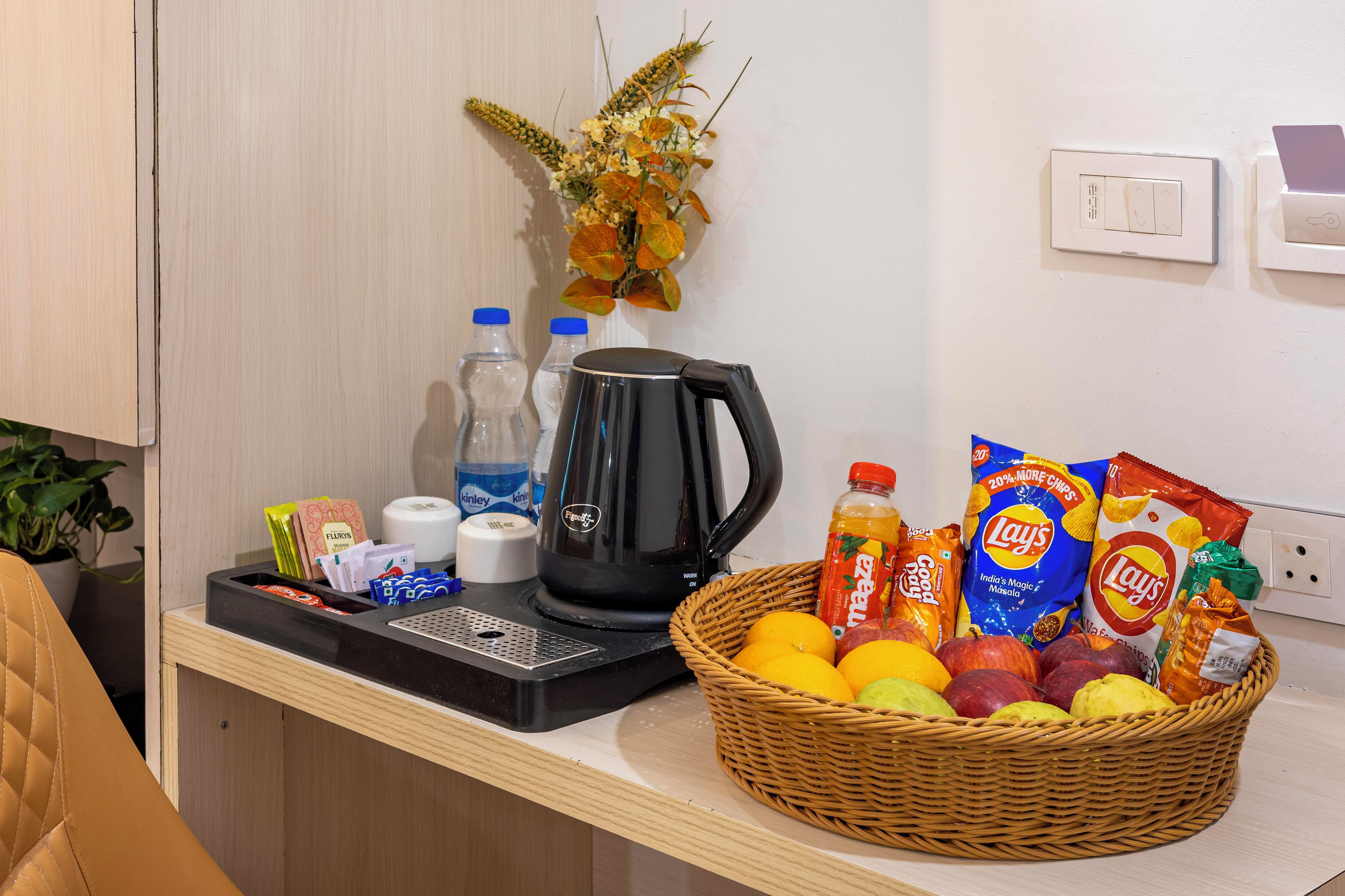 Uma bancada de cozinha com uma cafeteira, garrafas, uma cesta de frutas e lanches.