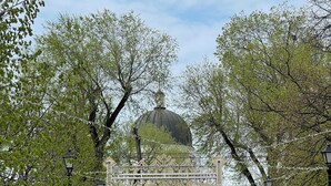Una plaza empedrada con una gran estructura en forma de cúpula al fondo, rodeada de árboles y farolas.