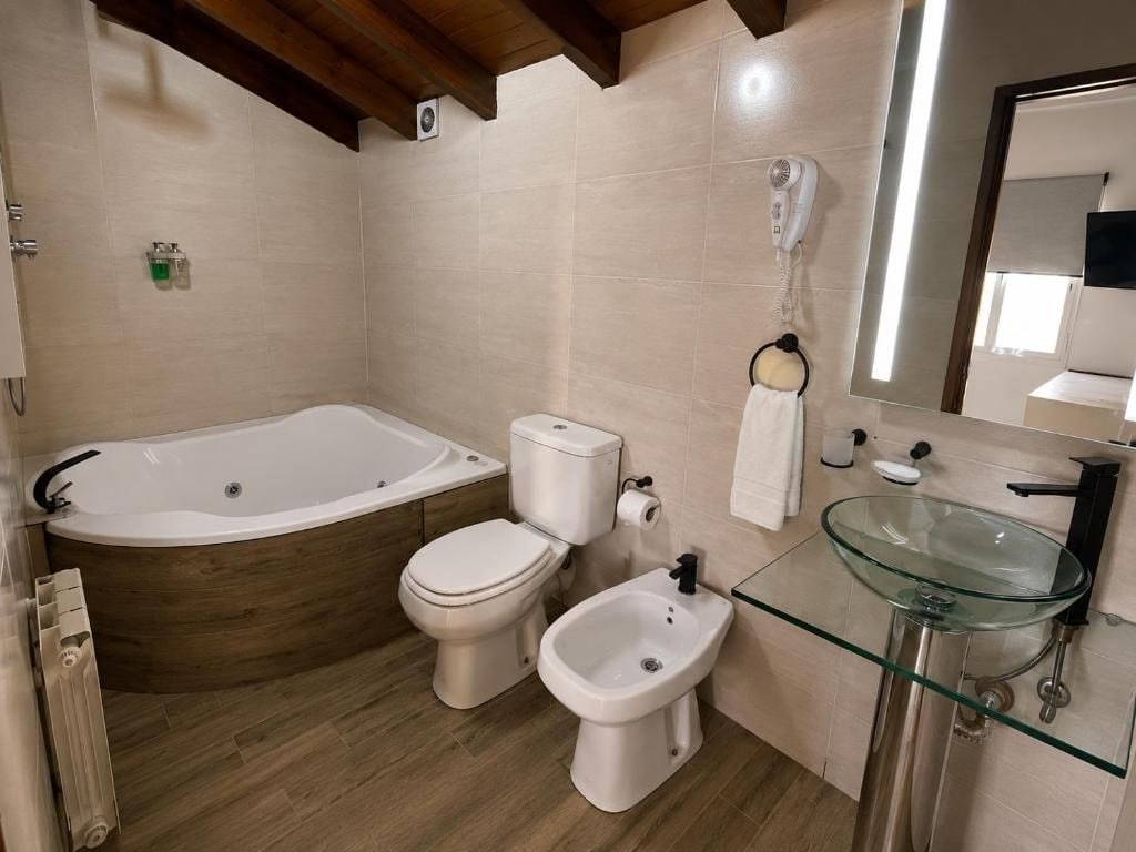 A bathroom with a bathtub, toilet, bidet, and glass-enclosed sink.