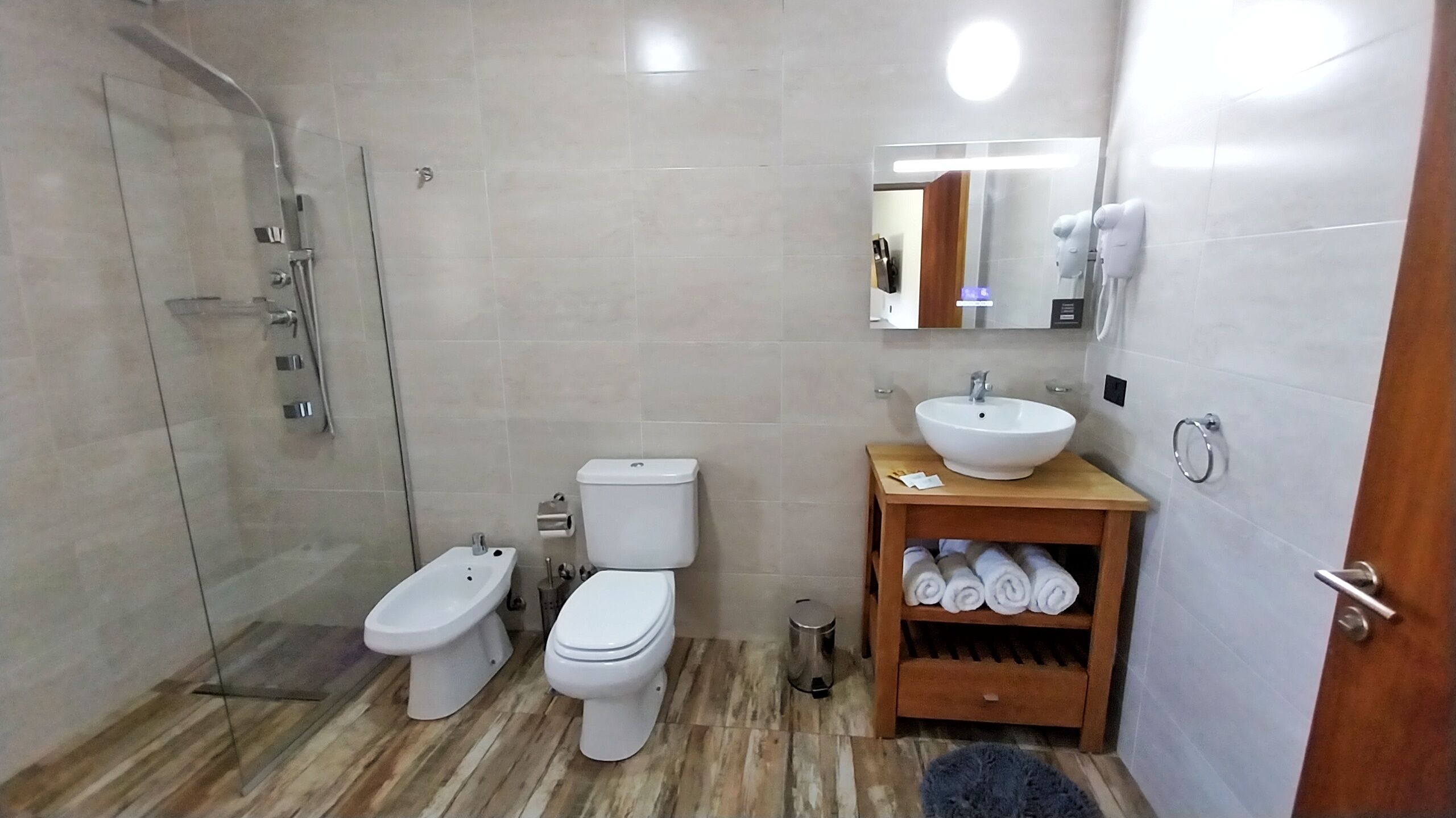 A bathroom with a glass shower enclosure, two toilets, a sink, and a mirror.