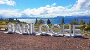 Large white letters spelling "BARILOCHE" on a gravel path with a scenic view of mountains and a lake in the background. - Las Victorias Suites Bariloche (San Carlos de Bariloche)