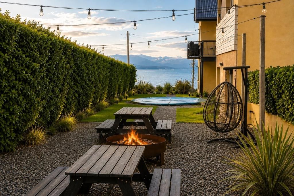 Un patio con mesas de madera y una chimenea, con vistas a un cuerpo de agua y montañas.