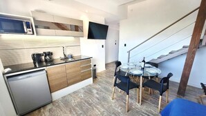Cocina compacta con lavavajillas, microondas y cafetera. Hay una zona de comedor con mesa y sillas.