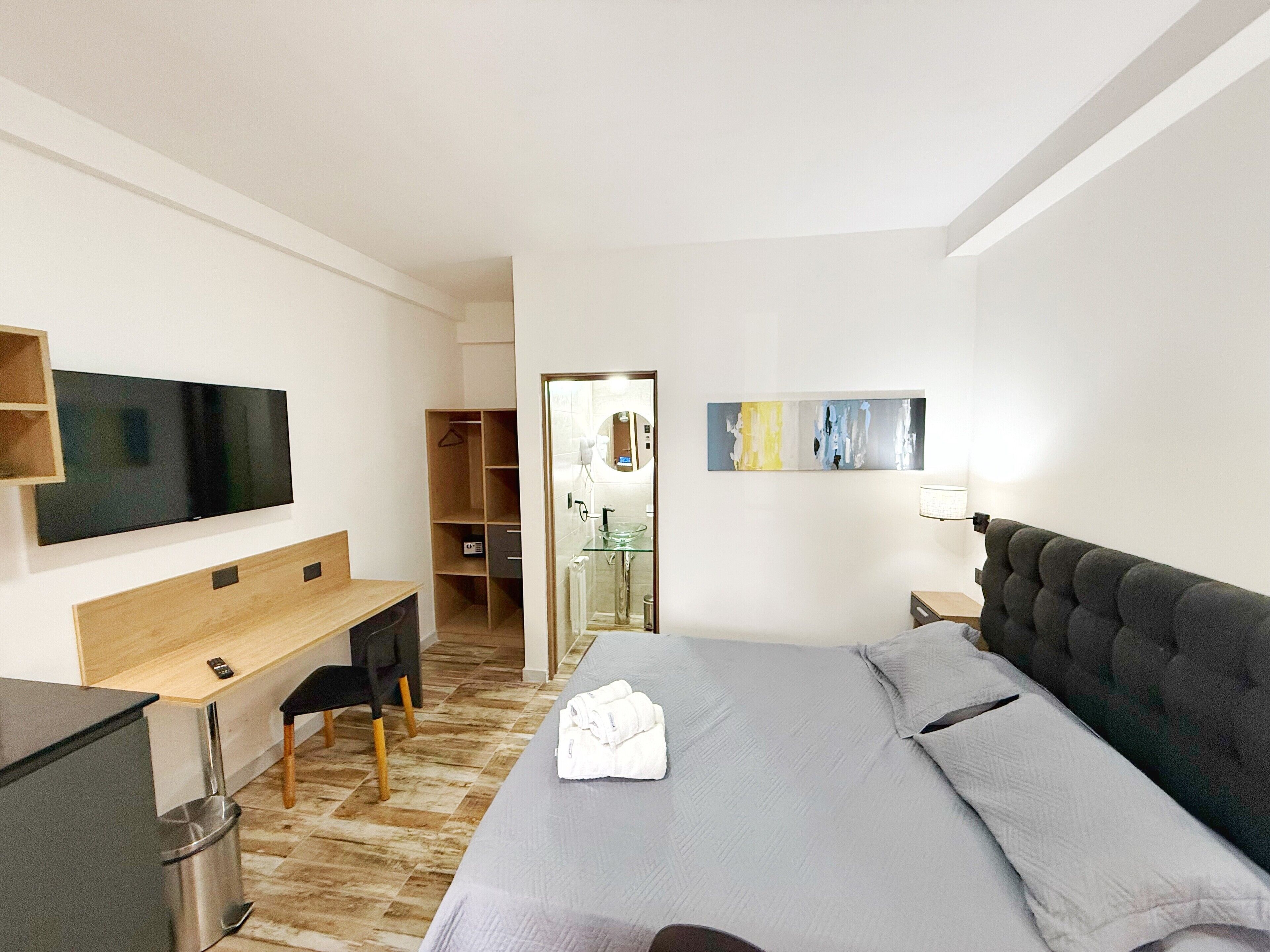 A modern hotel room with a bed, a desk, a TV, and a bathroom visible through an open door.