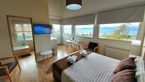 Habitación de hotel moderna con una cama grande, televisor, zona de comedor y vistas al mar.