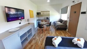 A compact hotel room with a TV, a dining area, a kitchenette, and a bed with towels. - Las Victorias Suites Bariloche (San Carlos de Bariloche)