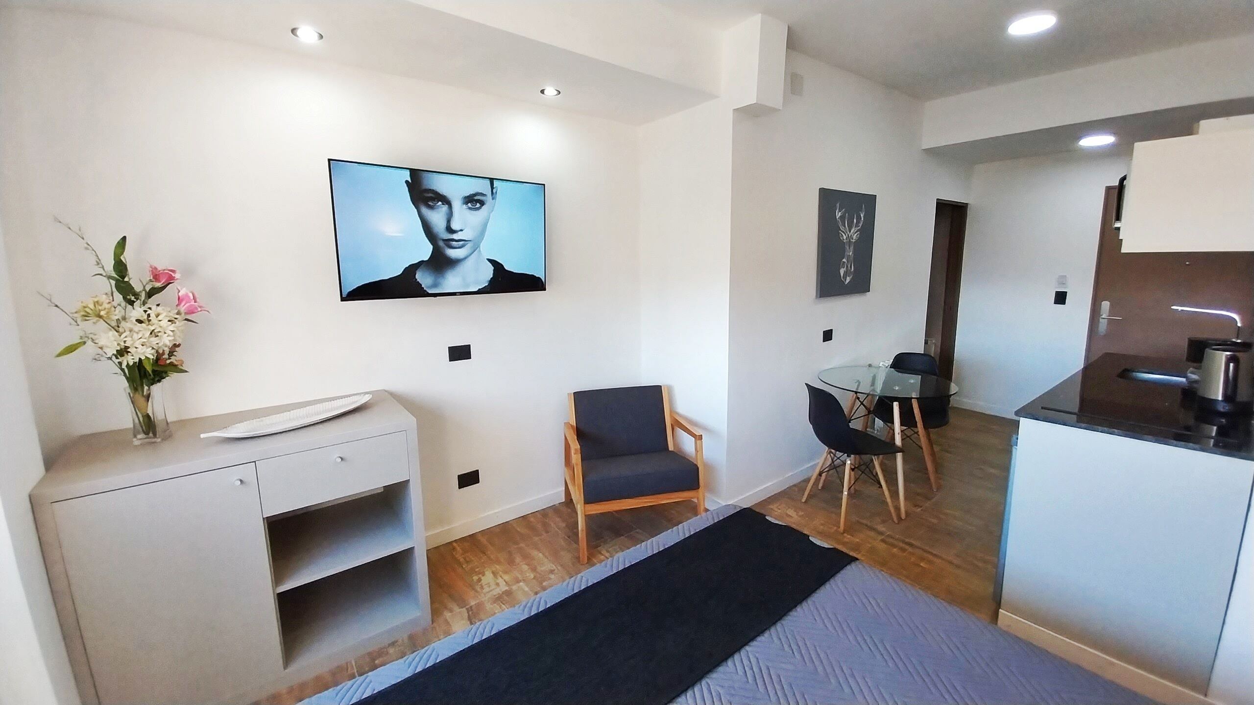A modern kitchen with a dining area, a small seating space, and a TV mounted on the wall.