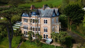 A large, multi-story building with a prominent tower, surrounded by lush greenery and a well-maintained garden. - Westwell Hall, large coastal house sleeping up to 29 (Ilfracombe)