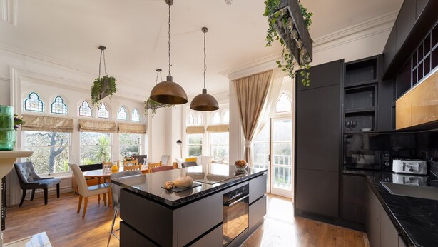 A modern kitchen with a central island, dark cabinetry, and pendant lighting. - Westwell Hall, large coastal house sleeping up to 29 (Ilfracombe)