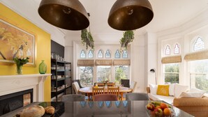 A dining area with a black marble table, surrounded by chairs, and a window with decorative stained glass. - Westwell Hall, large coastal house sleeping up to 29 (Ilfracombe)