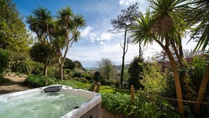 A hot tub surrounded by lush greenery and a view of a distant landscape. - Westwell Hall, large coastal house sleeping up to 29 (Ilfracombe)