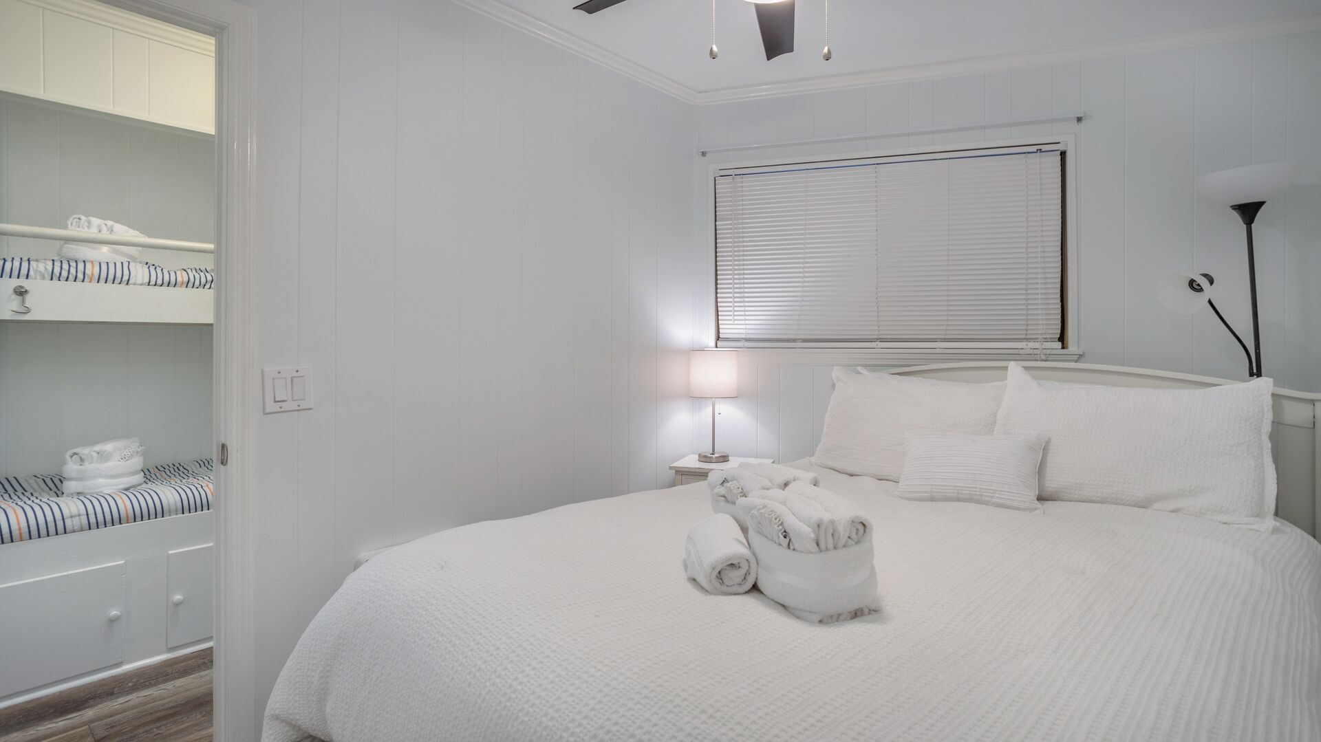 Ein Schlafzimmer mit Bett, Nachttisch mit Lampe, Jalousien am Fenster und einem Einbauschrank.