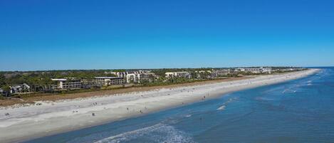A beach resort with multiple buildings along the shoreline, a sandy beach, and clear blue water.