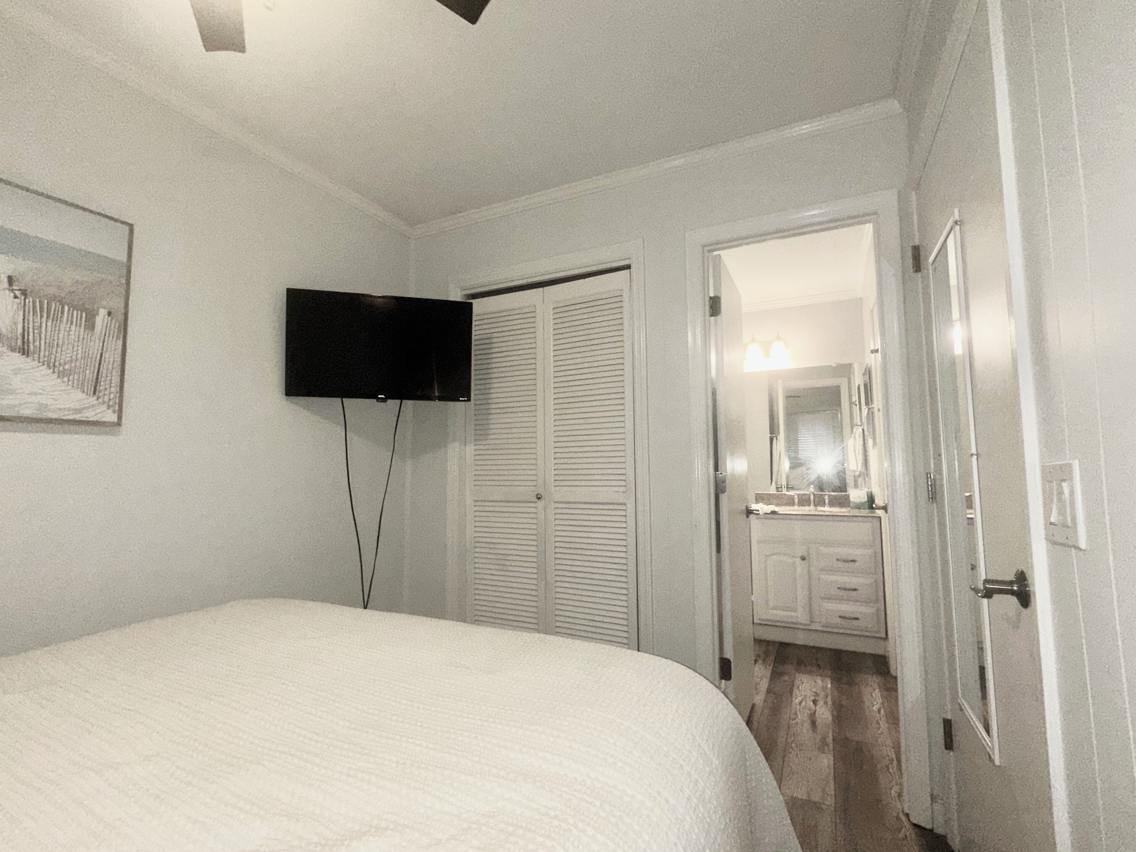 A bedroom with a bed, a television mounted on the wall, a closet, and a bathroom visible through an open door.