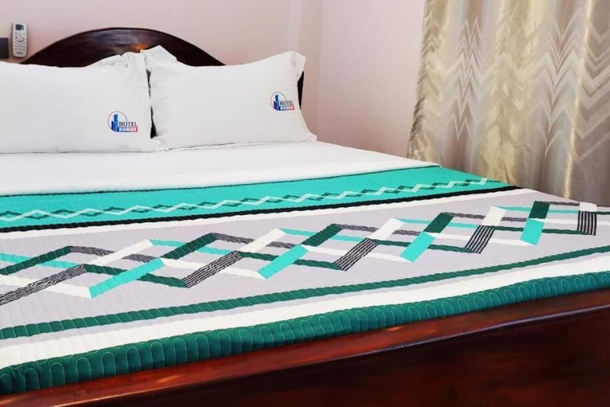 A bed with a patterned bedspread, two pillows, and a bedside table with a remote control.