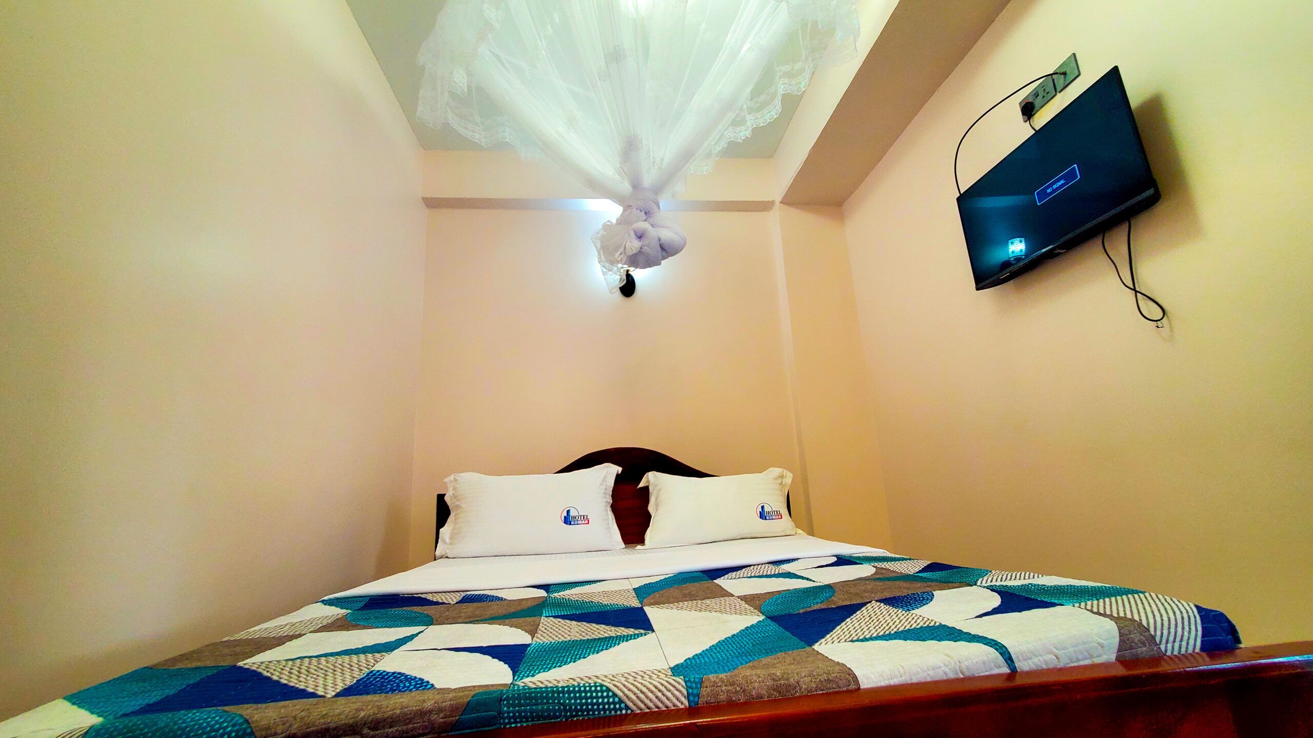 Een hotelkamer met een bed, een plafondventilator, een bevestigde televisie en een airconditioning.