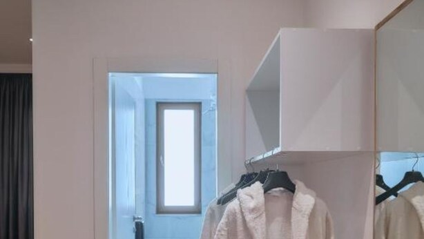 A hotel room with a wooden floor, a bed, a wardrobe, and a window.
