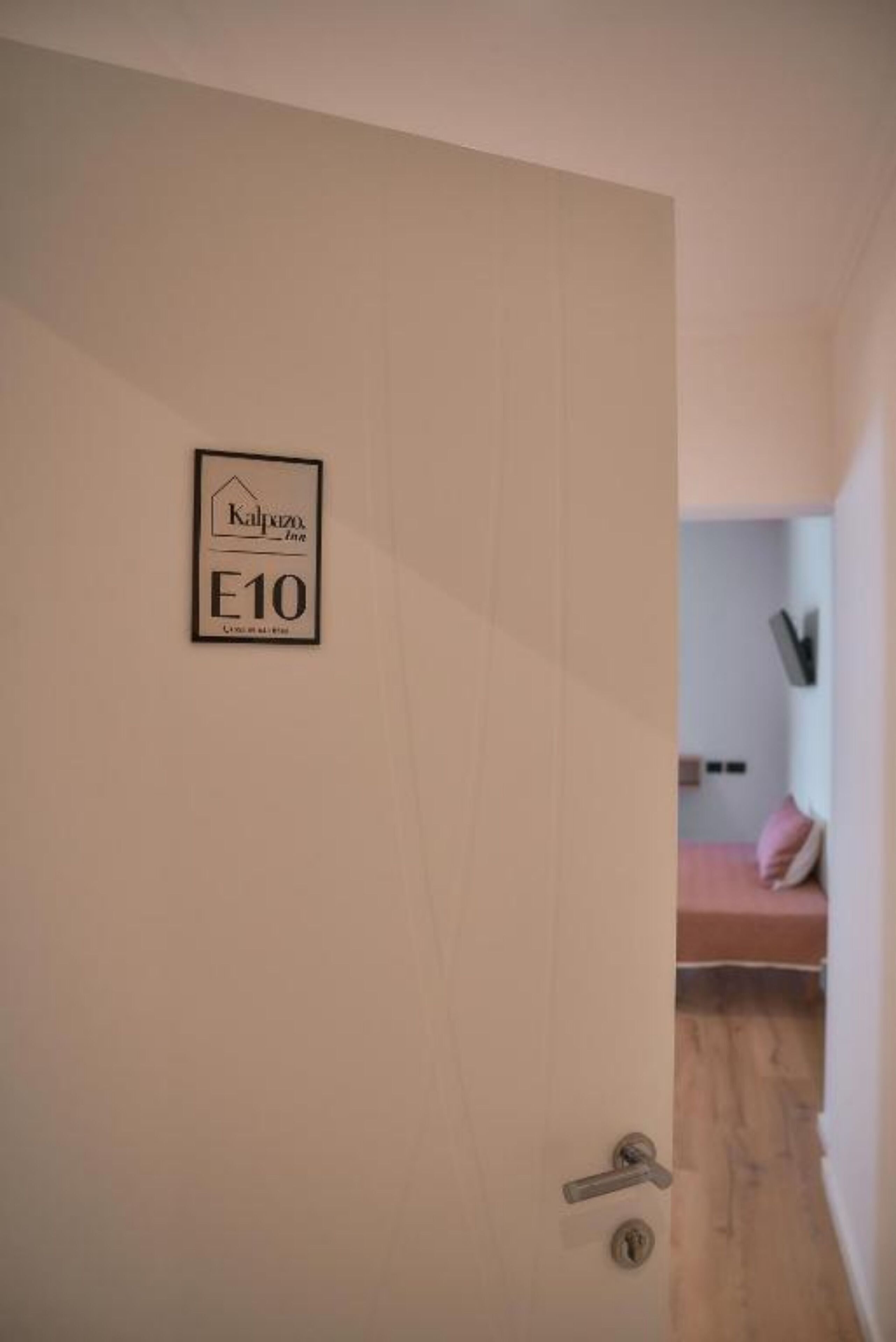 A hotel room with a door labeled "Kalypso Inn E10" and a bed with a pink pillow.