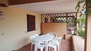 A covered patio with a white table and chairs, a brown door, and a metal fence. - THREE-ROOM APARTMENT RESIDENCE WITH SWIMMING POOL IN EXCLUSIVE AREA AND NEAR THE SEA (Porto Cervo)