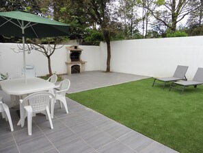 Eine Terrasse mit Tisch und Stühlen, einem Grill und einem Rasen.
