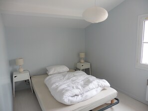 Ein schlicht eingerichtetes Schlafzimmer mit einem Einzelbett, zwei Nachttischen und einer Pendelleuchte.