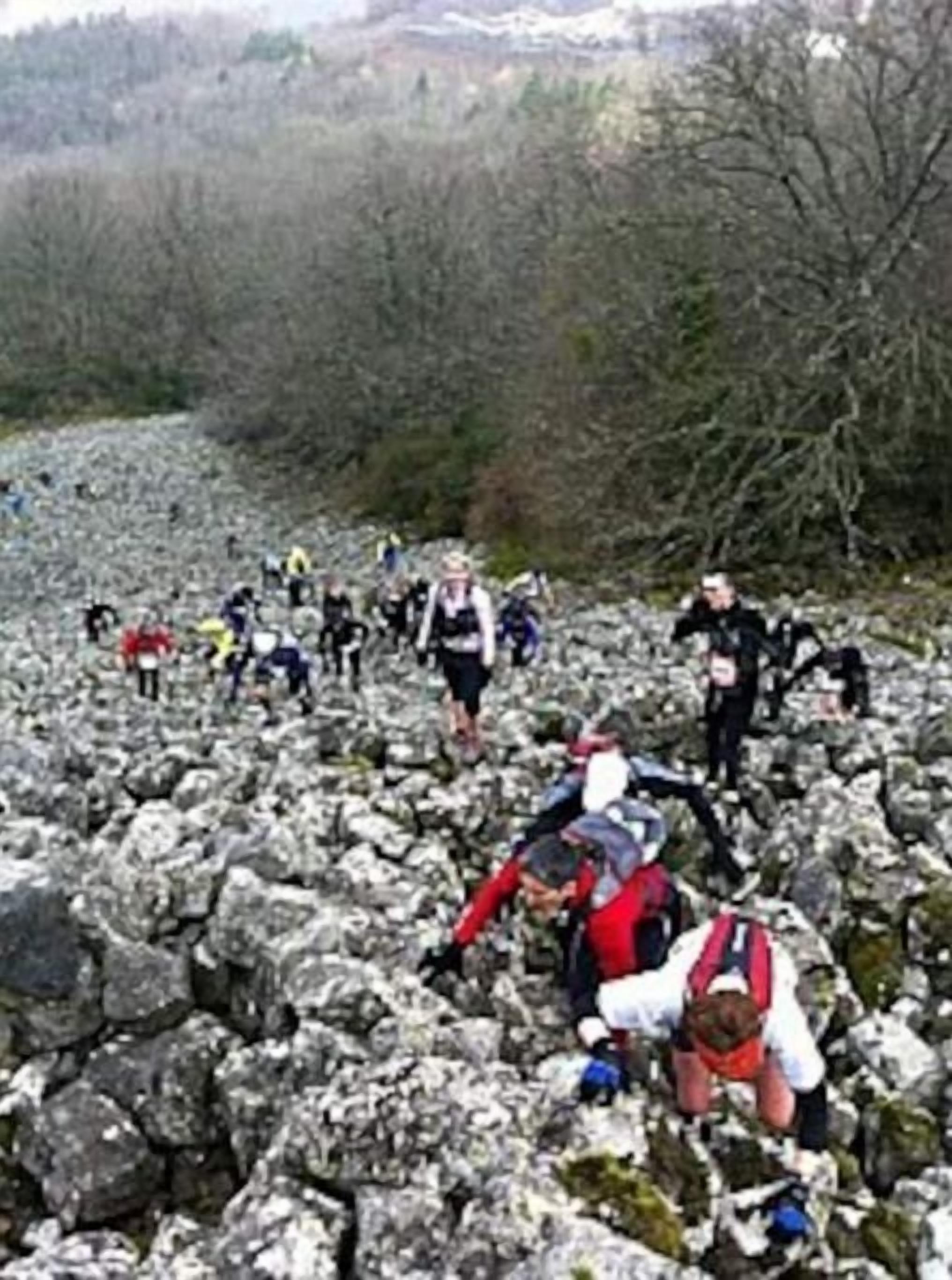 A group of people hiking on rocky terrain with sparse vegetation in the background.