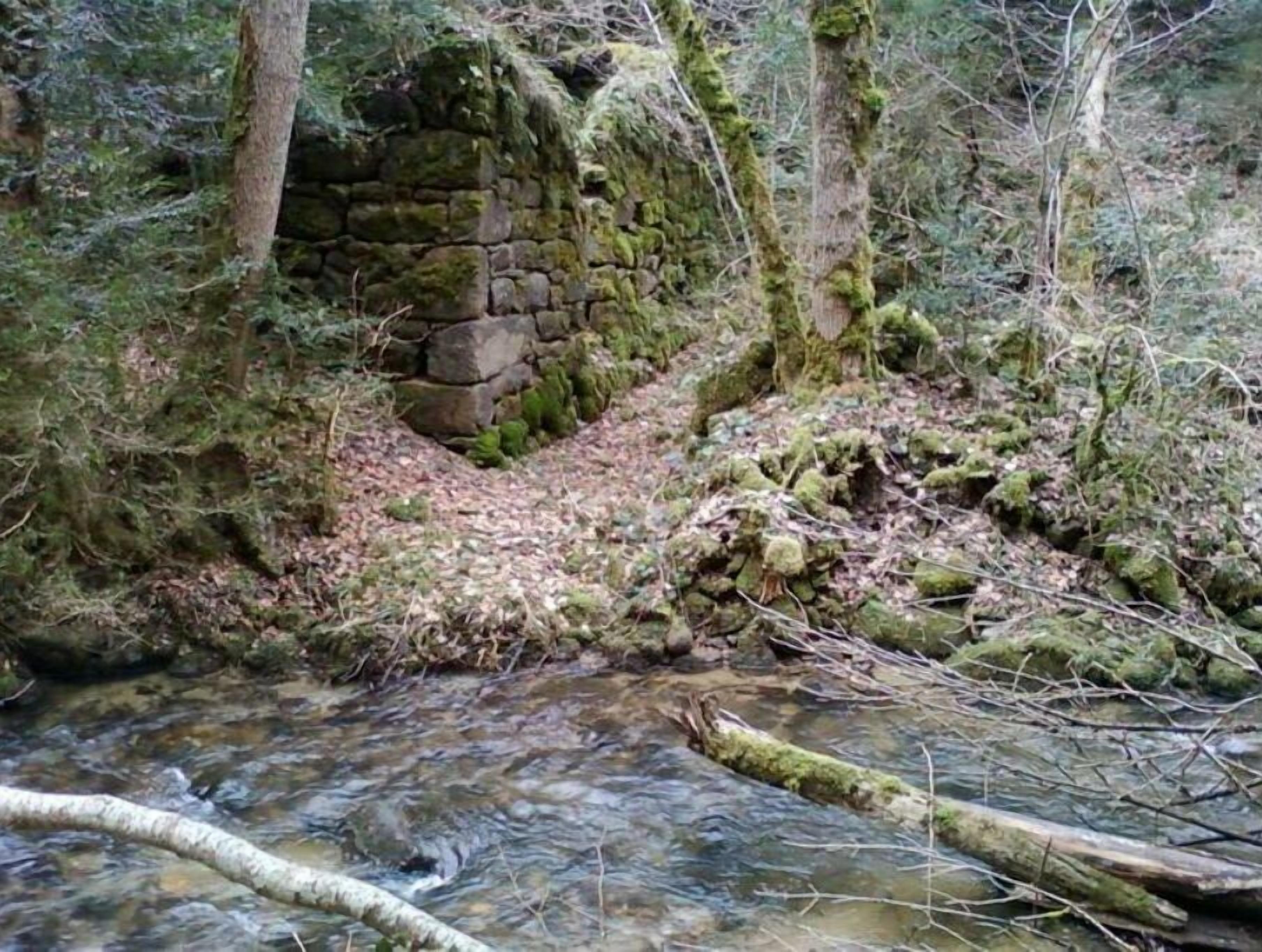 Una construcción de piedra en un área boscosa con un arroyo.