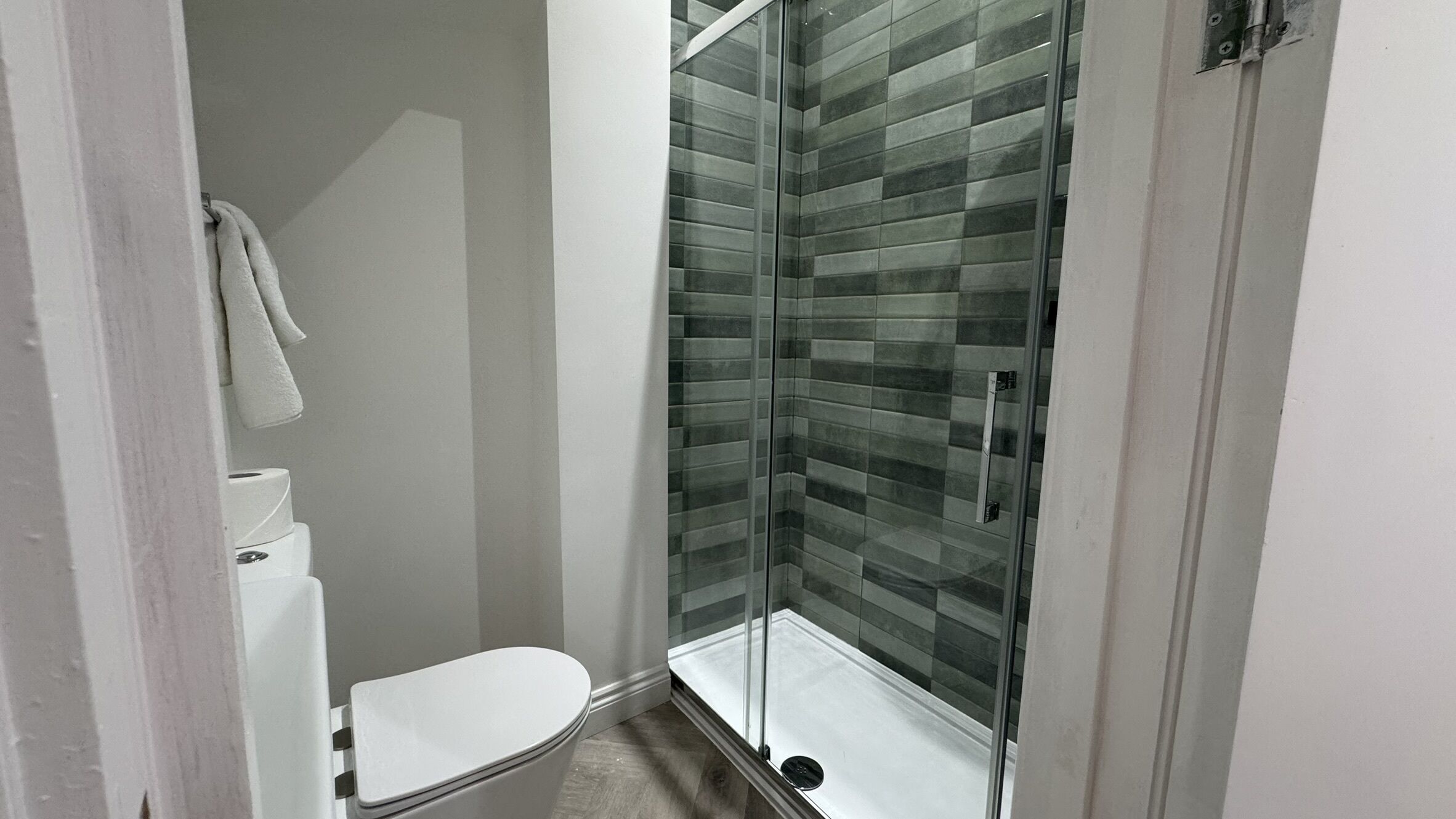 A small bathroom with a toilet, a glass shower enclosure, and a towel hanging on the wall.