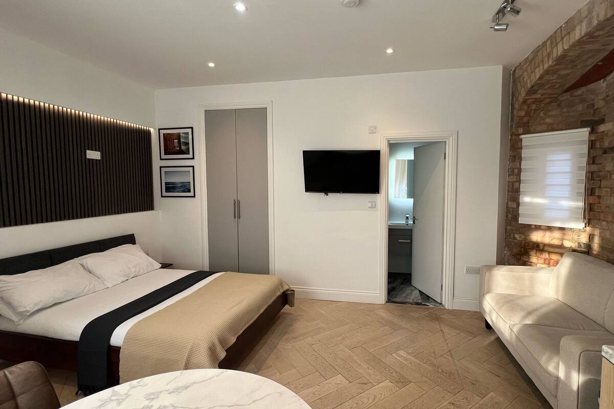 A modern bedroom with a bed, a sofa, a TV, and a brick wall.