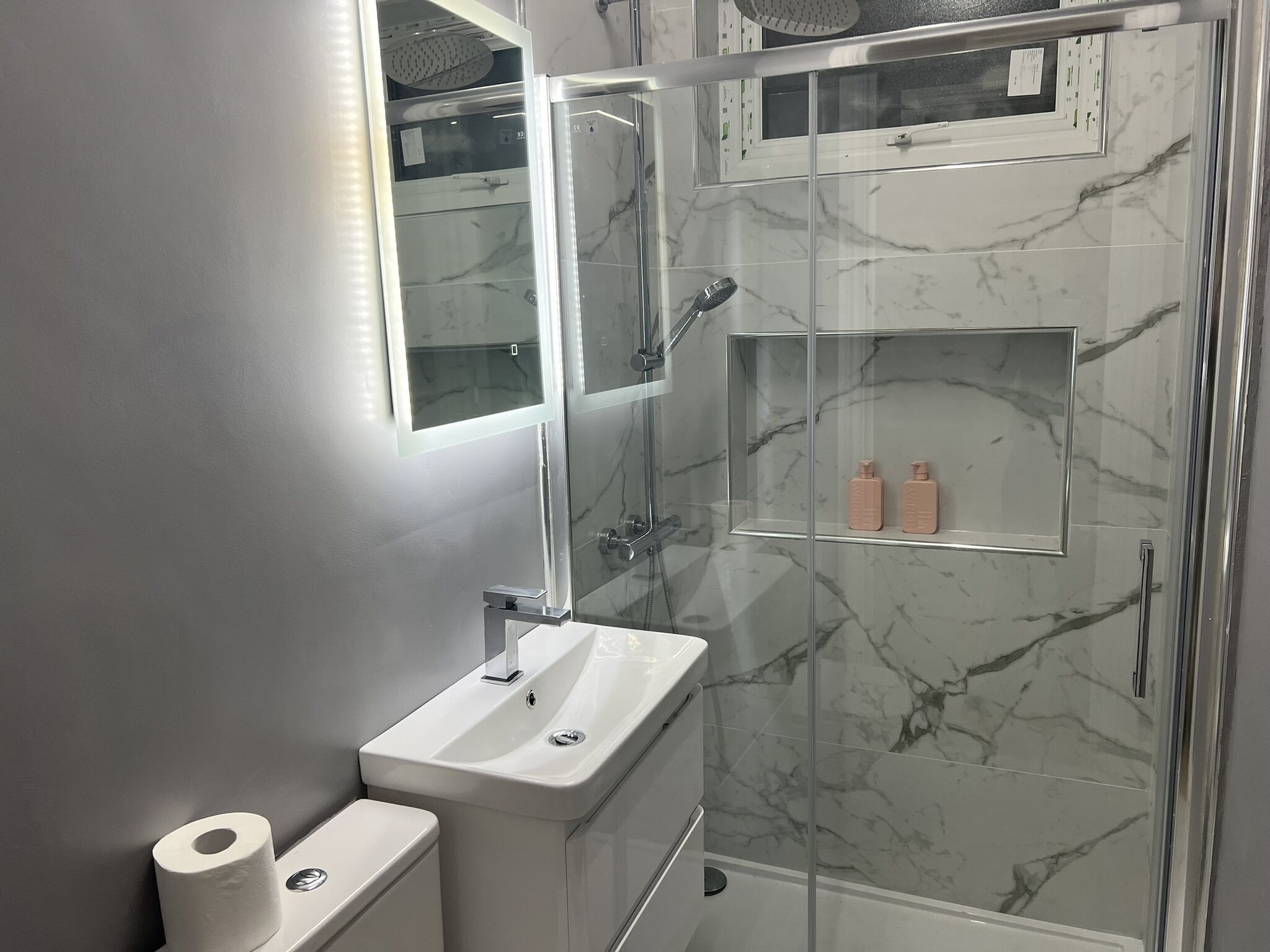 A modern bathroom with a glass-enclosed shower, a white sink, and a marble backsplash.