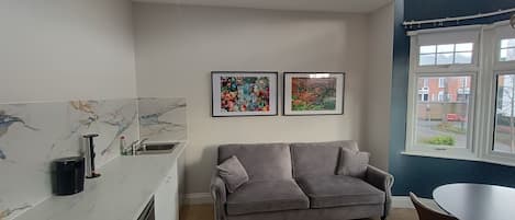 A modern kitchen with a marble countertop, a grey sofa, and two framed artworks on the wall.