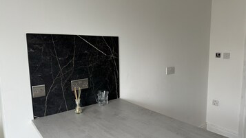 Una habitación con pared de mármol, suelo gris y una peque ña mesa con un vaso y una botella.