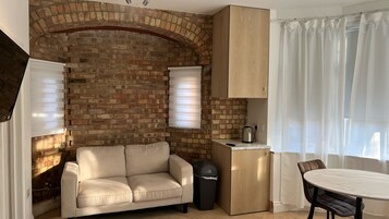 Un espacio habitable compacto con pared de ladrillo, un sofá, una mesita y un armario.