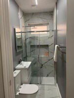 A compact bathroom with a glass shower enclosure, a white sink, and a toilet.