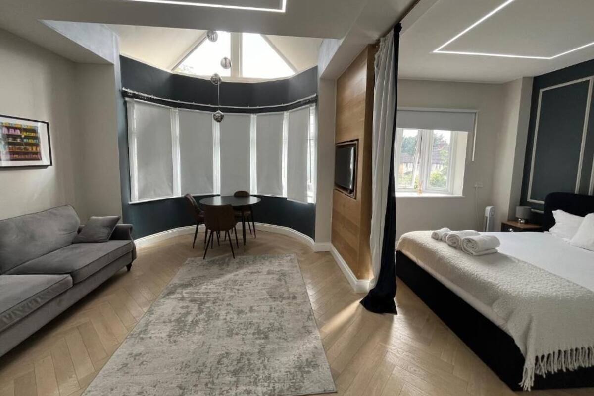 A modern bedroom with a bed, a sofa, a dining table, and a large window.