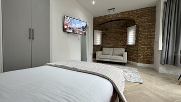 A bedroom with a bed, a TV mounted on the wall, a sofa, and a brick wall.