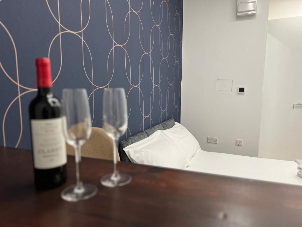 Ein Hotelzimmer mit einem Bett, einem Nachttisch mit einer Weinflasche und Gläsern sowie einer Wand mit Muster.