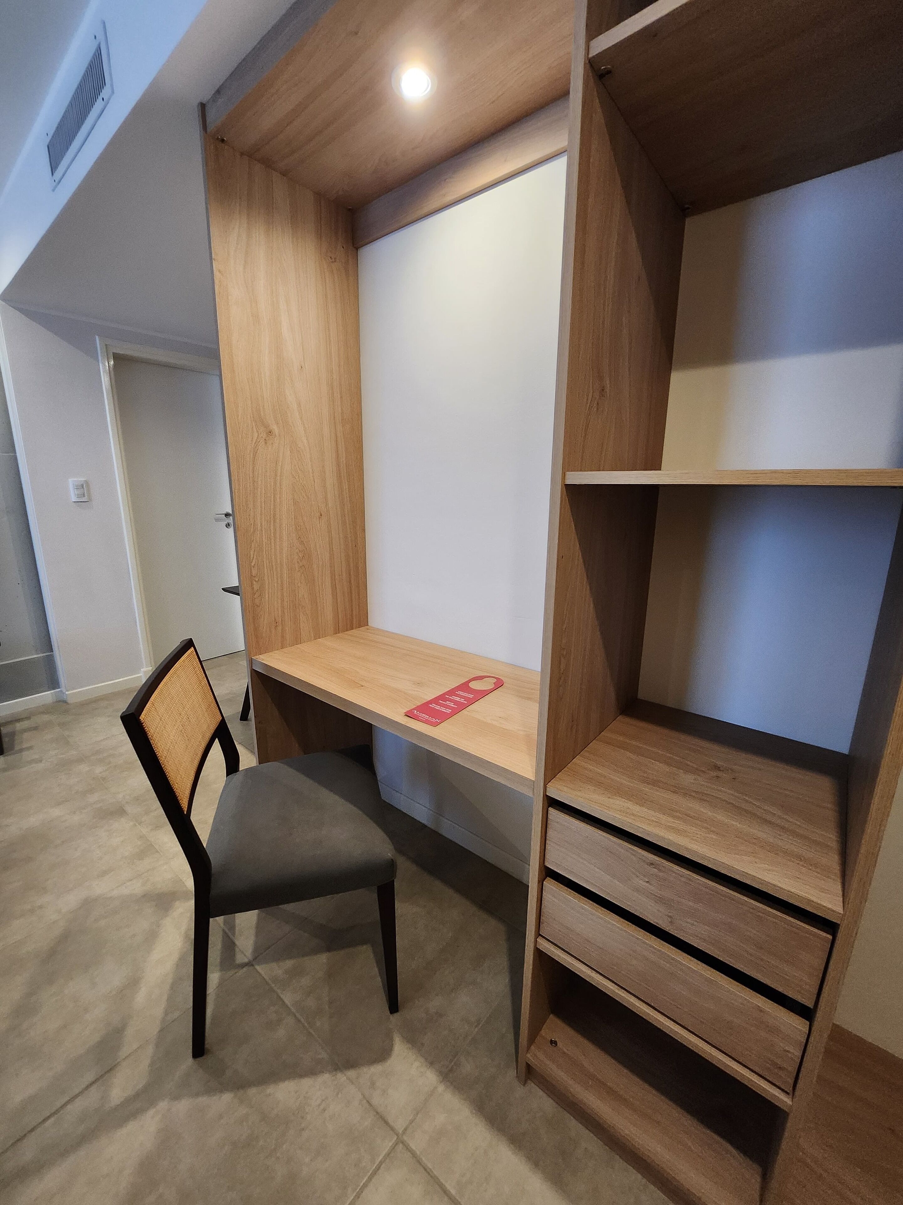 Quarto moderno com escrivaninha embutida, uma cadeira e estante.