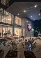 Una entrada moderna a un edificio con fachada de vidrio, un logotipo destacado en la pared y un camino bien iluminado que lleva a la entrada.