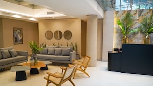 A modern lobby with a grey sofa, wooden chairs, a coffee table, and a reception desk. - Amerian Rio Cuarto (Rio Cuarto)