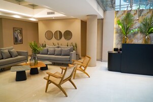 Un moderno vestíbulo con un sofá gris, sillas de madera, una mesa de centro y un mostrador de recepción.