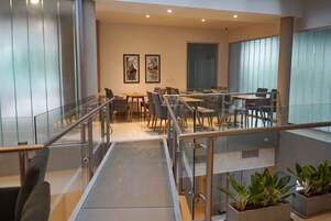 Un moderno vestíbulo de hotel con una escalera de cristal, zona de estar y plantas en macetas.
